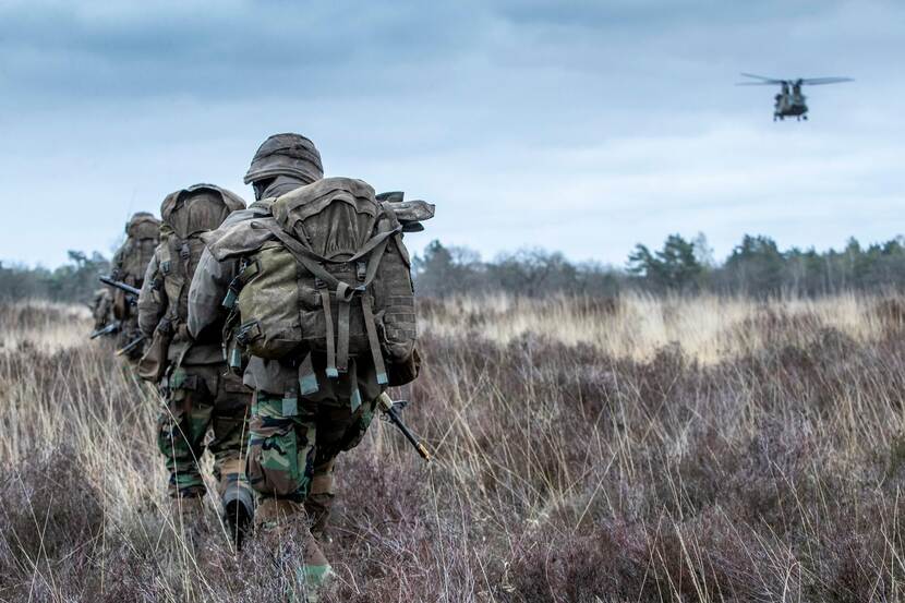 Rij mariniers loopt door landelijk gebied, Chinook in de verte.