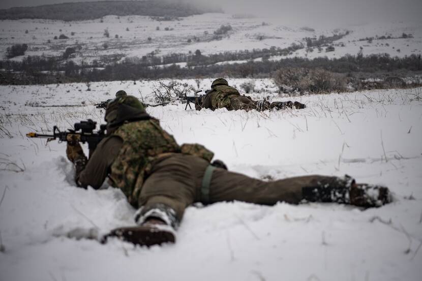 2 militairen op de grond in de sneeuw met wapen.