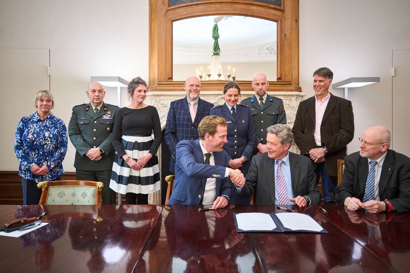 Handen worden geschud na de ondertekening. Mensen staan erachter.