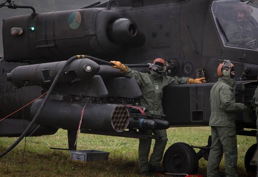 Militairen staan voor een Apache-gevechtshelikopter met geleide raketten.