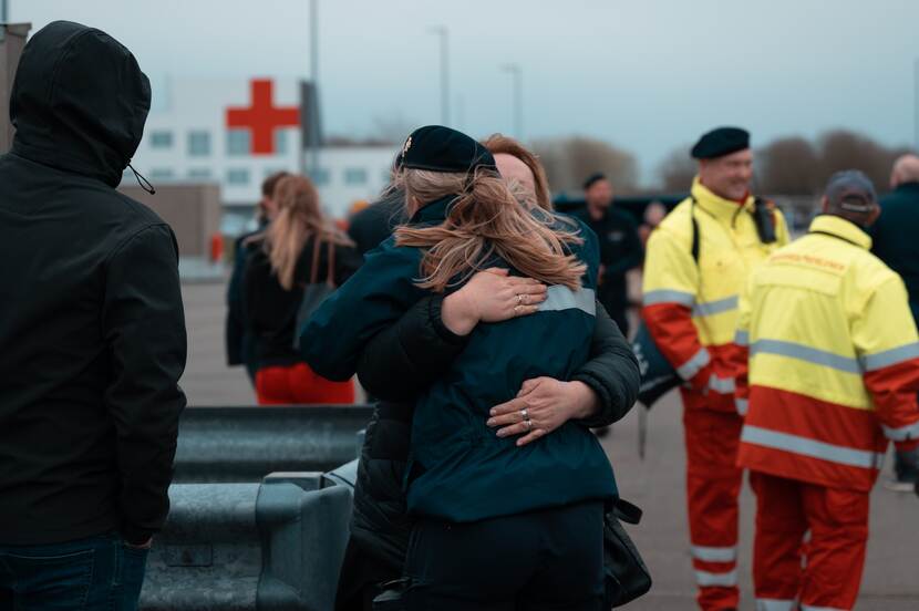 Mensen op de kade, onder wie 2 vrouwen die elkaar omhelzen.