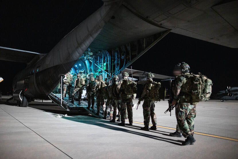 Militairen lopen een C-130 Hercules-transportvliegtuig in, klaar voor een evacuatieoperatie.