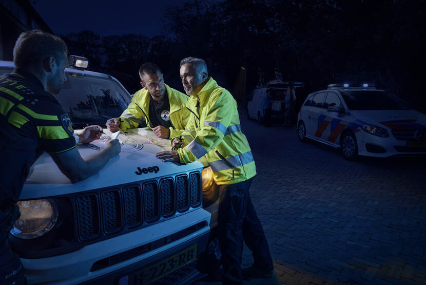 Defensie-veteranen en politieagent in het donker in gesprek, leunend op een Jeep.