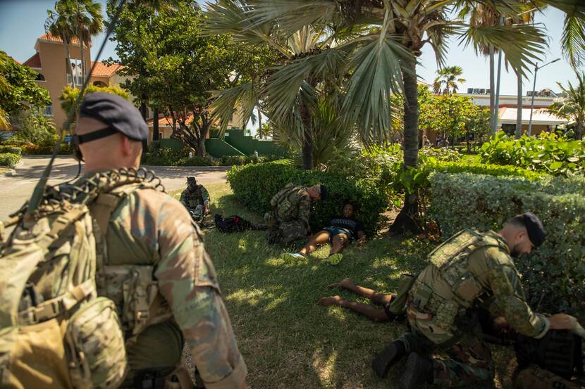 Militairen verzorgen gewonden die in het gras liggen.