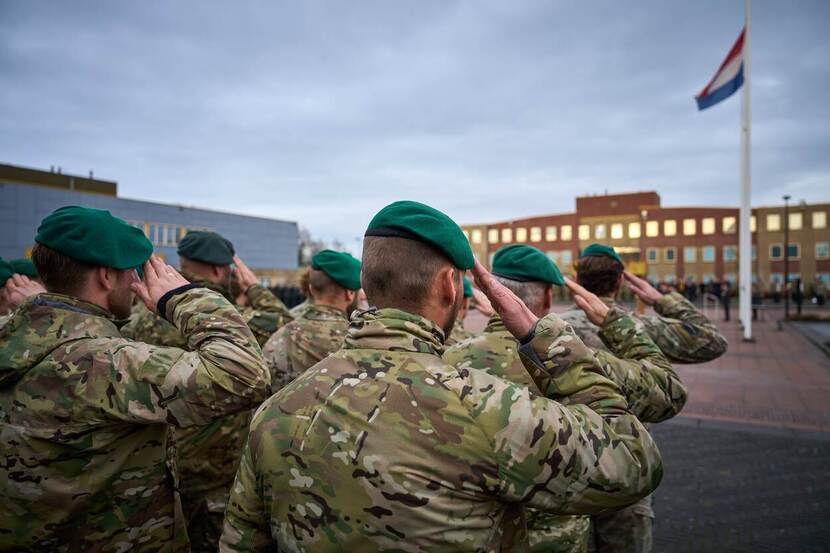 Groep saluerende commando's op de rug gezien, met de Nederlandse vlag in top.