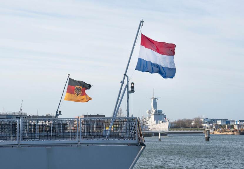 Duitse en Nederlandse vlag wapperen op achtersteven van een marineschip.