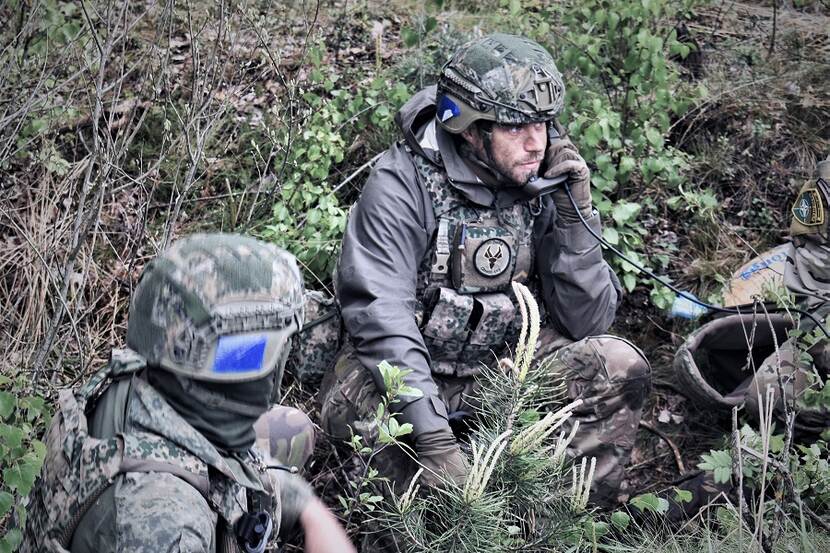 2 militairen met radio zitten in groen landschap.