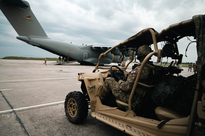 Voertuig met militair staat geparkeerd voor een militair vliegtuig.