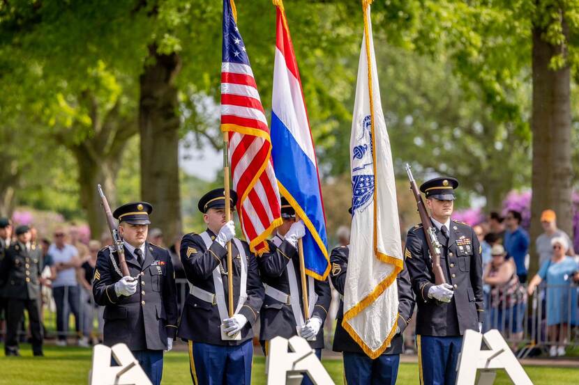 5 militairen met vlaggen en wapens.