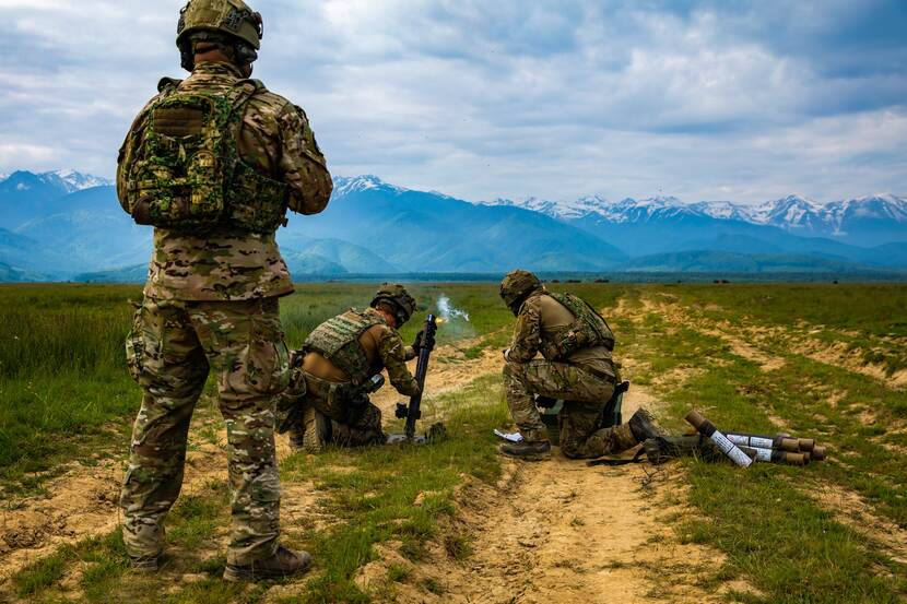 Militairen schieten wapen af. Achtergrond bergen in felblauw licht onder de wolken.