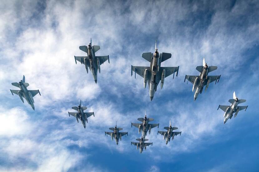 Onderaanzicht van een formatie van 10 Nederlandse F-16's, tegen een blauwe lucht.