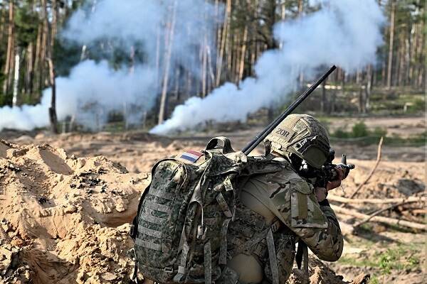 Gewapende militair op de rug gezien met op de achtergrond rookpluimen in een bos.