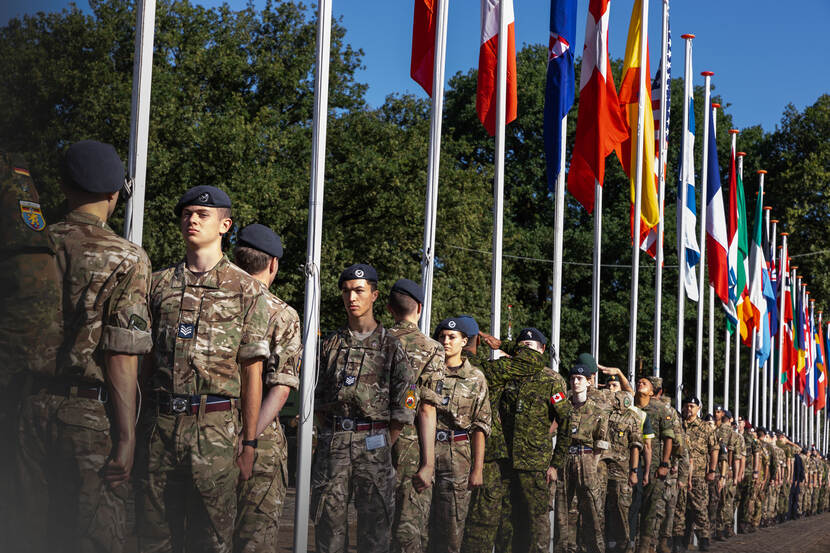 Militairen staan opgesteld onder landenvlaggen.