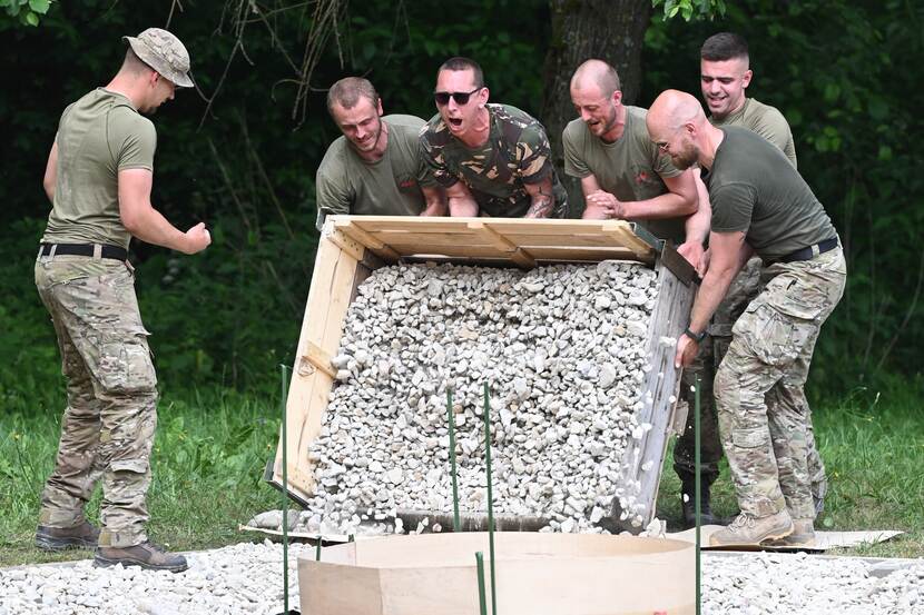 Groep militairen stort bak met grind op de grond.