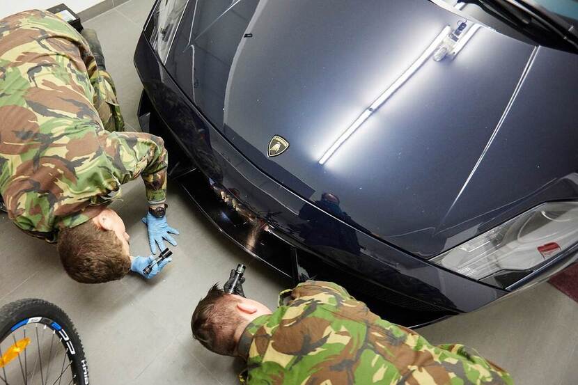 2 militairen schijnen met zaklampen onder een zwarte auto.