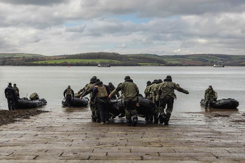 Mariniers dragen een rhib naar zee. 3 rhib's liggen al in het water.