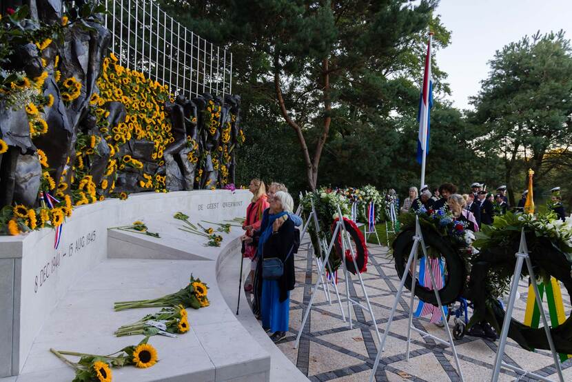 Mensen staan voor het met monument, waarop zonnebloemen liggen.