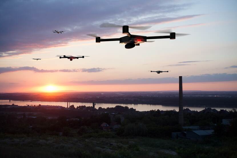 Een zwerm drones vliegt in de lucht bij zonssondergang.