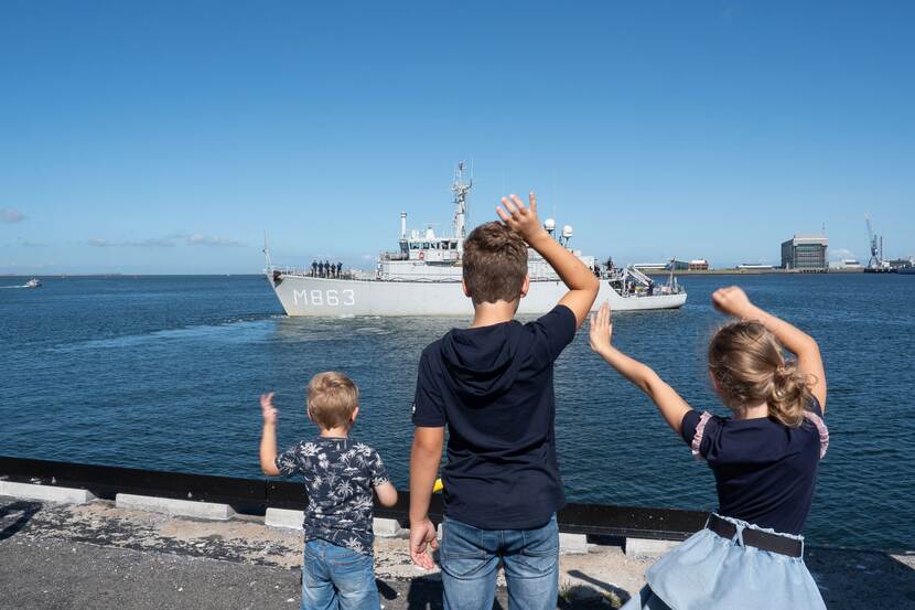 3 kinderen zwaaien naar uitvarend marineschip.