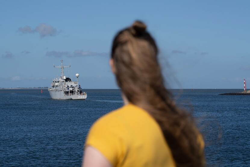 Vrouw kijkt naar uitvarend marineschip.