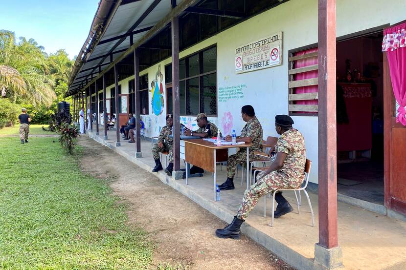 Surinaamse militairen zitten op stoelen en achter een tafel voor een medisch centrum.