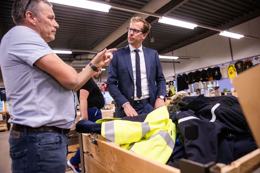 De staatssecretaris krijgt een toelichting bij een houten bak met kleding.