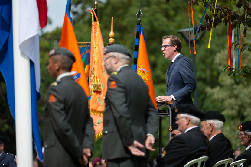 Van der Maat houdt een toespraak. Naast hem staan en zitten veteranen.