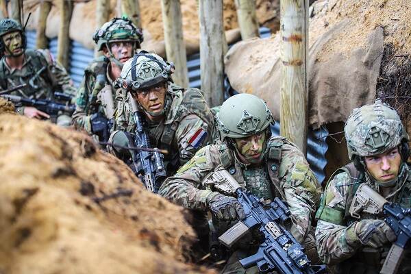 5 gecamoufleerde militairen met wapen in een loopgraaf.