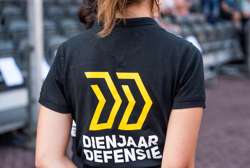 Meisje op de rug gezien met op de achterkant van haar T-shirt de tekst Dienjaar Defensie.