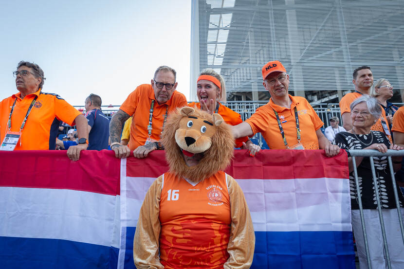 Familie moedigt atleten aan. Grote oranje leeuw staat voor hen.