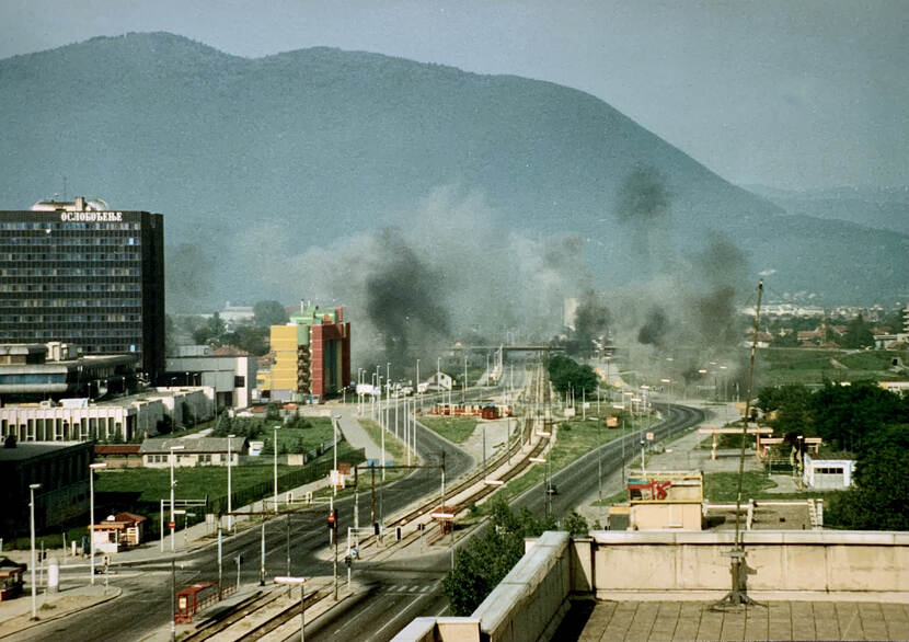 Archieffoto van een spoorbaan in een stad tijdens inzet in voormalig Joegoslavië. Zwarte rookpluimen stijgen op.