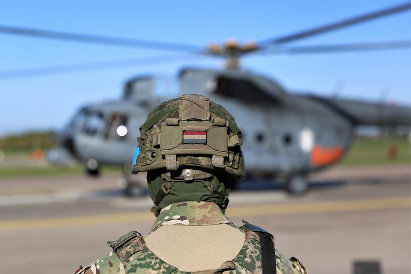 Een Nederlandse militair op de rug gezien, achter hem een helikopter.
