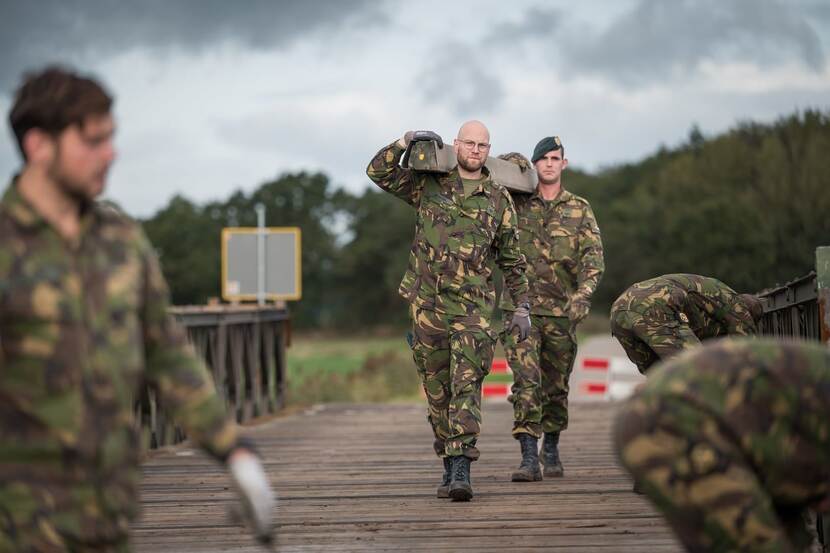 Militairen sjouwen met materiaal op brug.