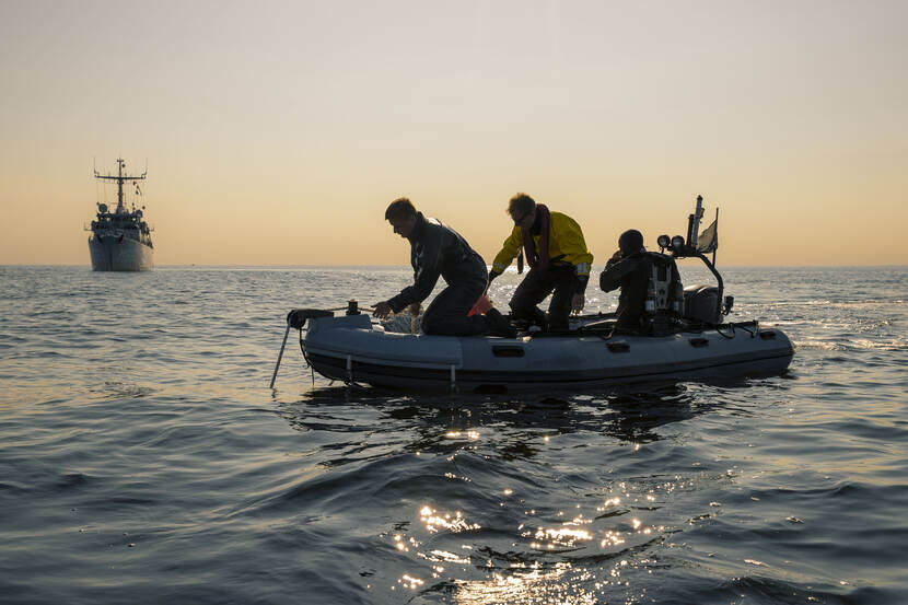 Marineduikers in een rubberboot op zee, op de achtergrond Zr.Ms. Vlaardingen.