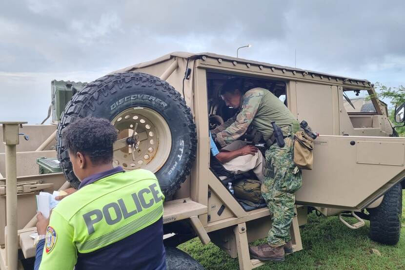 Militair op St. Maarten helpt iemand in een auto. Politieman op de voorgrond.