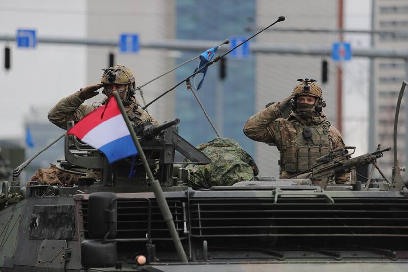 2 militairen op een militair voertuig. Voorop wappert Nederlands vlaggetje.