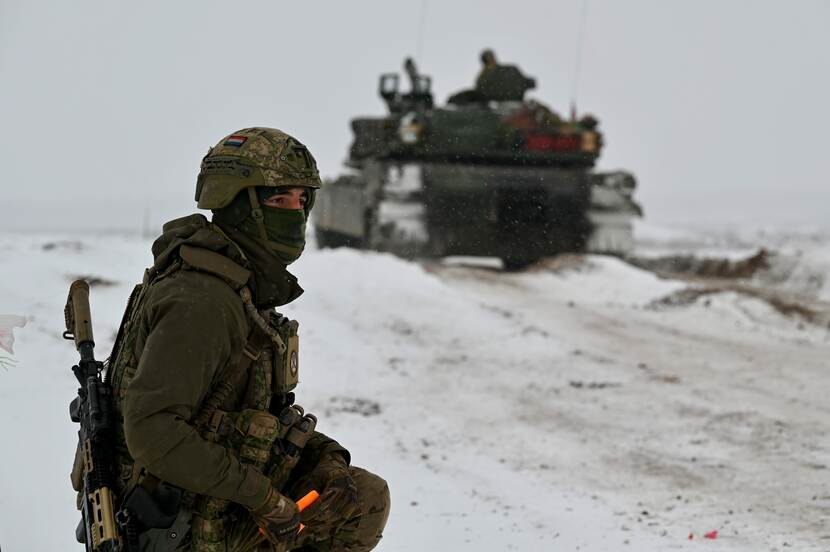 Militair in sneeuw met tank op de achtergrond.