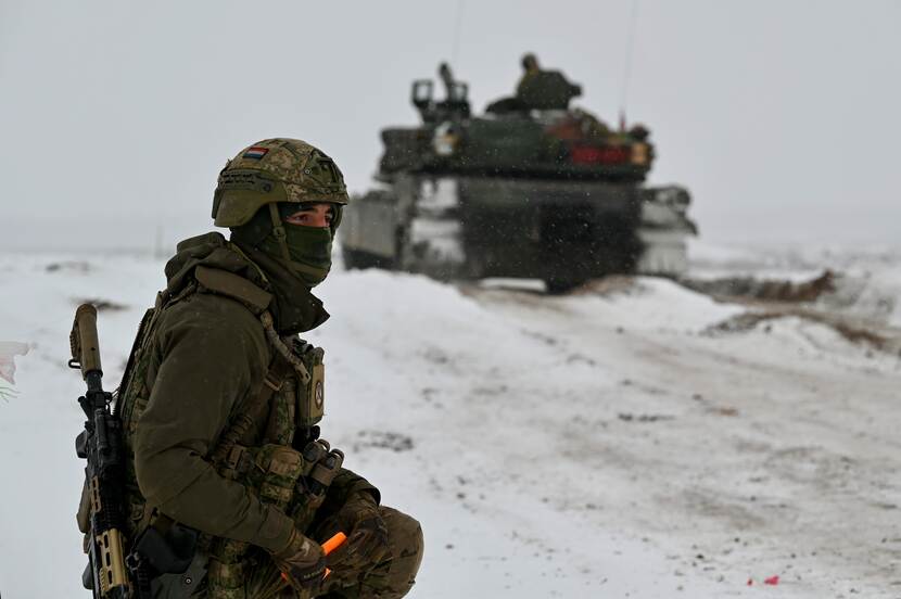 Militair in de sneeuw met een tank op de achtergrond.