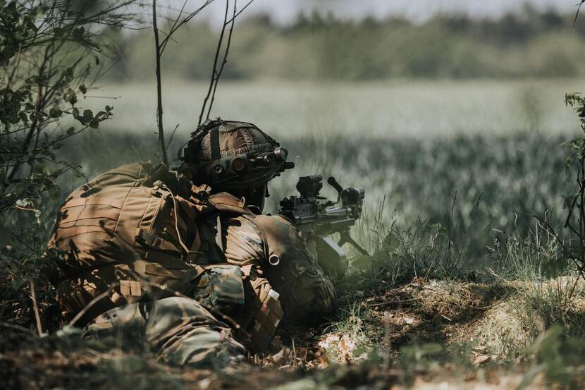 Bewapende militair ligt in het veld.