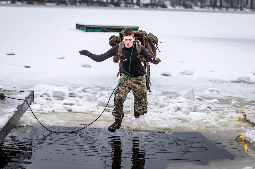 Militair met bepakking springt in een wak.