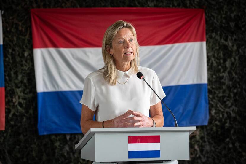 Ollongren achter katheder, met de Nederlandse vlag achter haar.