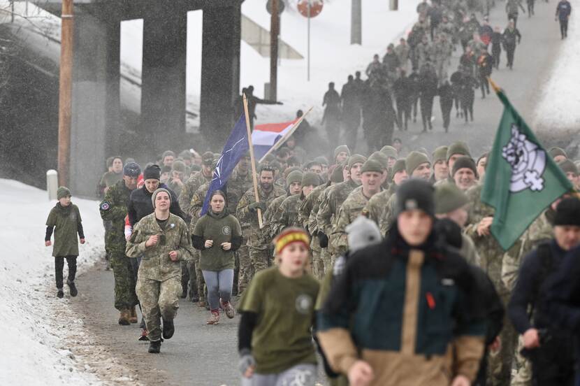 Lange rij hardlopende burgers en militairen tegen besneeuwde achtergrond.