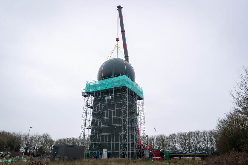 Een mobiele hijskraan plaatst een geluidwerende koepel op het militaire radarstation in het Friese Wier. Het radarstation staat in de steigers.