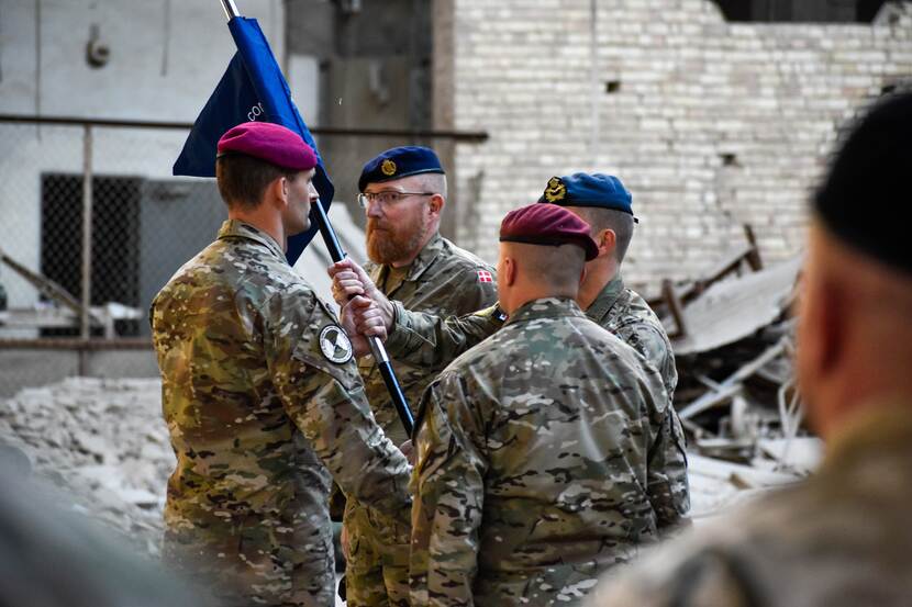 Deense militair overhandigt NMI-vlag aan Nederlandse militair.