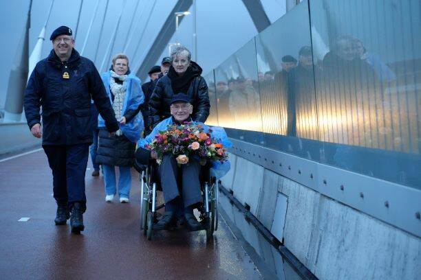 Bewoners en personeel van Bronbeek lopen bij zonsondergang over de brug De Oversteek.