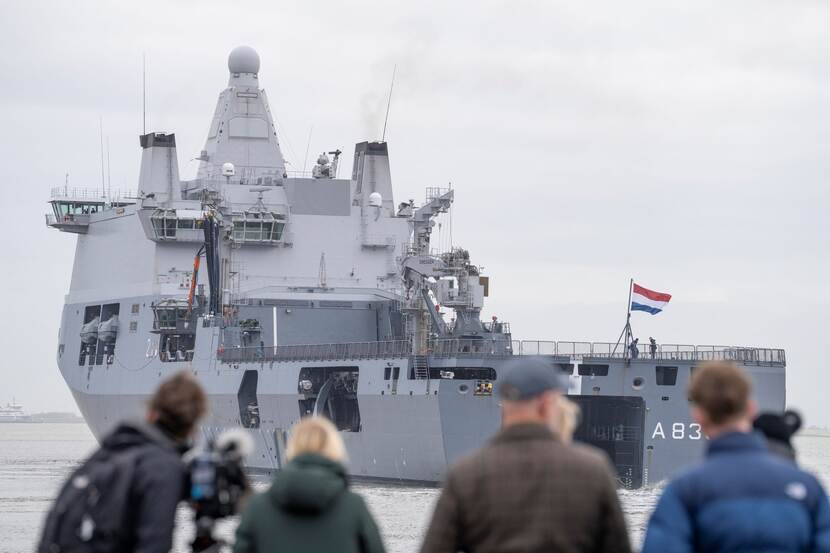 Mensen op de kade kijken naar een uitvarend marineschip