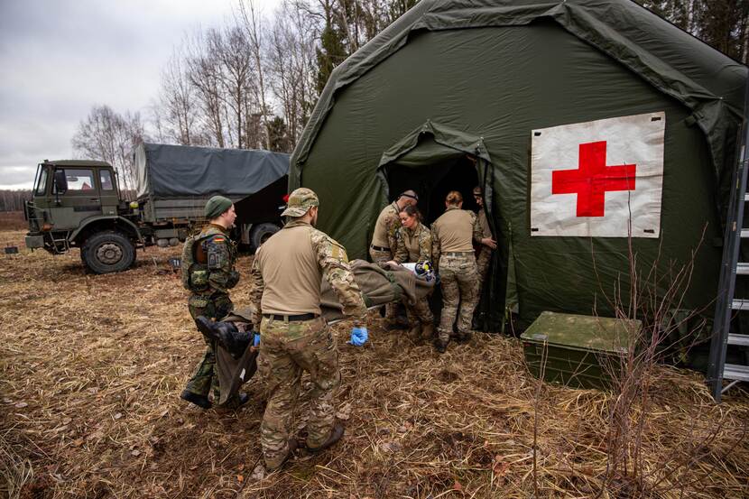 Legertent met rood kruis. Gewonde militair wordt naar binnen gedragen.