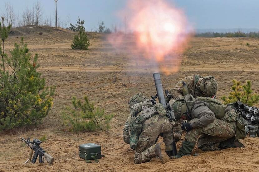 Militairen schieten liggend op de grond een mortier af. Vuurwolk.