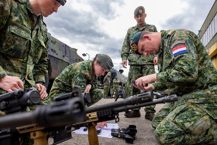 3 landmachtmilitairen controleren wapens. Een vierde kijkt toe.