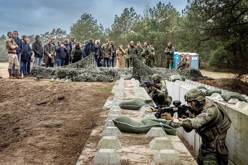 Militairen in loopgraven. Groep burgers kijkt ernaar.